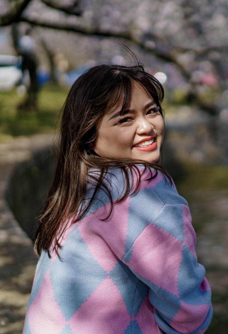 Jessica smiling in front of cherry blossom trees and a pond by the Tidal Basin in Washington DC